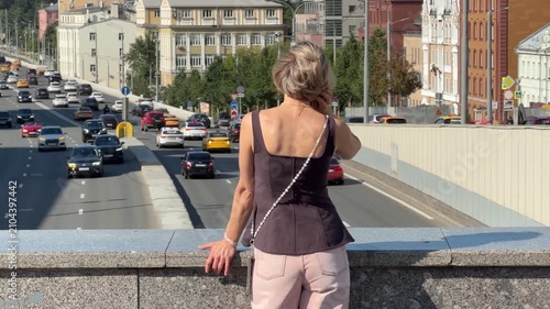 Stylish woman enjoys sunny day in Moscow overlooking busy city avenue from urban viewpoint with relaxed confident expression. Lifestyle, travel, urban living, freedom, tourism, city exploration