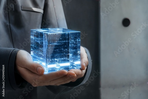 Close up of a glowing blue transparent data cube held by a person in a gray uniform, brutalist concrete background, cold sterile light, macro photography.