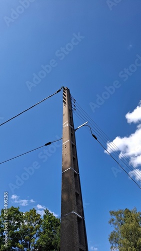 Concrete utility pole and overhead power lines against a blue sky with copy space