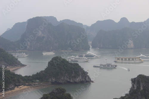 Tour boats navigate lush green limestone karsts in misty ha long bay vietnam.