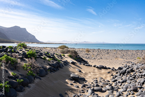Konstfotografi Dry desert beach landscape featuring black volcanic rocks, golden sand, clear oc