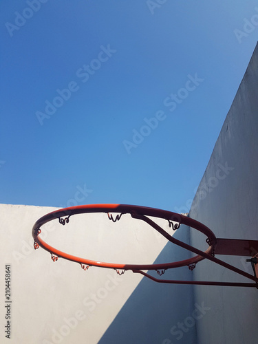 Minimalist outdoor basketball hoop against a clear blue sky with modern concrete walls creating geometric shadows.