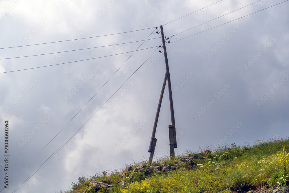 Fototapeta premium Utility pole on hill with wires against overcast sky