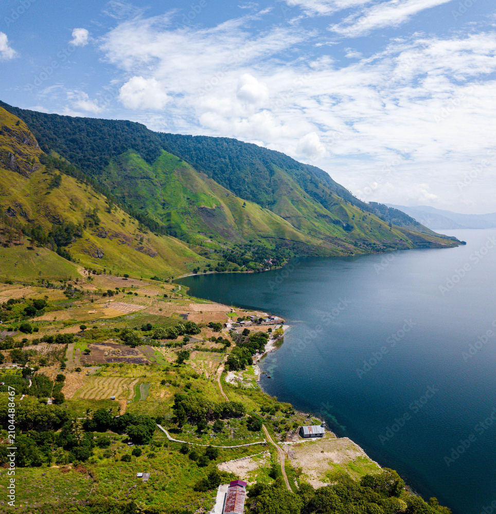Fototapeta premium Aerial drone view of serene lakeside with Batak village scenery near Toba Lake at Silalahi in Desa Binangara, Samosir, Sumatra Utara, Indonesia