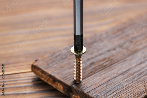 Foto Screwdriver on the screw, screw screwed into timber wood, screw on wooden top table