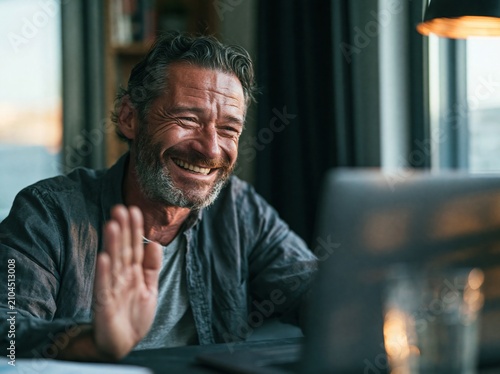 Man video calling from a laptop in a tidy home office during daylight hours