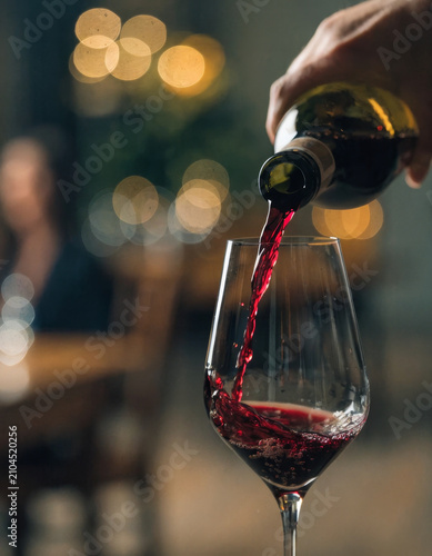 Hand pouring crimson red wine into crystal glass elegant atmosphere blurred background warm lighting celebration relaxation fine dining evening luxury enjoyment