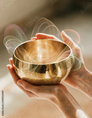 Close up of two hands holding polished brass singing bowl soft light spiritual energy meditation relaxation mindfulness wellness peaceful atmosphere