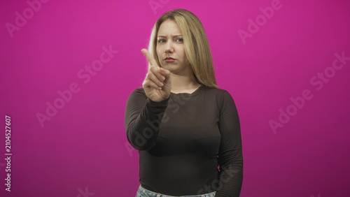 Canvastavla Woman points index finger forward with stern face, wearing black long sleeve top and jeans, blonde hair visible in studio; warning assertiveness