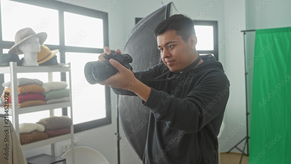 Fototapeta premium Man holding camera and adjusting lens in studio with green screen and reflector; creative concentration.