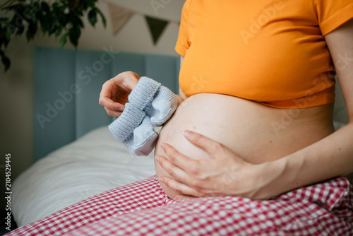 фотографія Pregnant woman anticipating motherhood, holding blue baby booties against her be