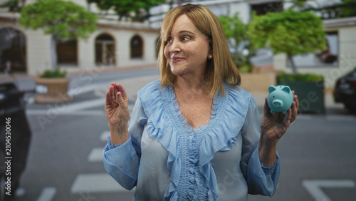 Konstfotografi Woman holding turquoise piggy bank in right hand and pinching fingers gesture on a street; saving prudence