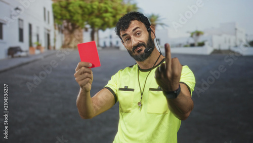 Cuadro en lienzo Man referee holding red card and showing middle finger on a street with whistle and headset visible; defiance