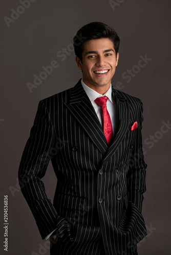 Portrait of a confident handsome young businessman in a black pinstripe suit and red tie smiling warmly