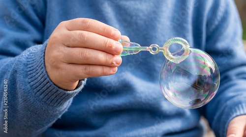 Close-up of Child's Hand Holding a Wand and Blowing Soap Bubbles