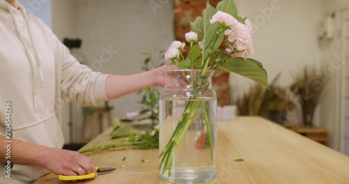 Floral composition. Bouquet arrangement. Unrecognizable female florist cutting flowers placing hydrangea in glass vase for home decoration.