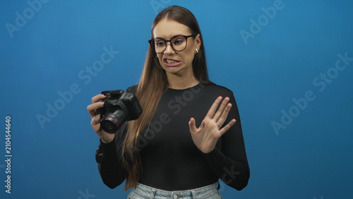 Konstfotografi Woman holding dslr camera with raised hand and grimacing face showing disgust while checking lens in studio; disgust rejection