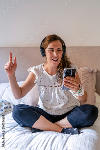 Obraz na płótnie A cheerful mid-adult woman raising her finger while listening to music through h