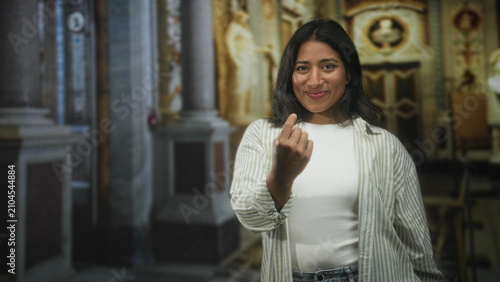 Schilderij op canvas Woman showing middle finger gesture with bare hand and slight smile while wearing white shirt and striped overshirt in ornate building interior; defiance