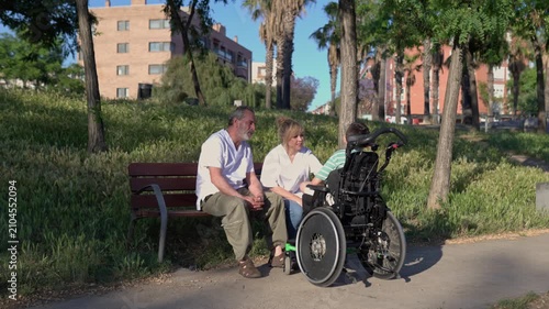 Caregivers assisting disabled child in wheelchair outdoors