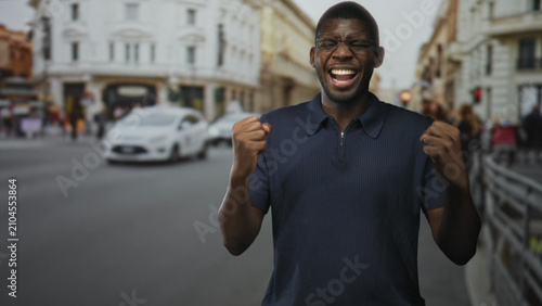 Photography Man with clenched fists shouting and laughing on a busy european street, wearing glasses and navy polo, mouth open in victory across a brief sequence; triumph joy