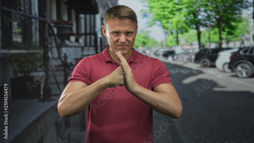 Принти на полотні Man pressing hands together in a tense gesture on a street with parked cars, stoop and trees; anger confrontation
