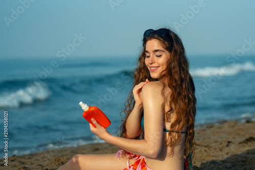 Photography Happy young woman enjoying relaxing beach vacation while applying sunscreen, sea