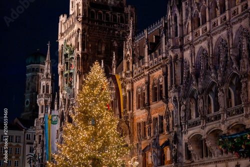 Illuminated Christmas tree in front of the historic New Town Hall at Marienplatz in Munich, Germany, with Frauenkirche dome visible at night