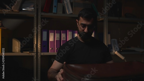 Foto Bearded man seated in a dim office with shelves behind