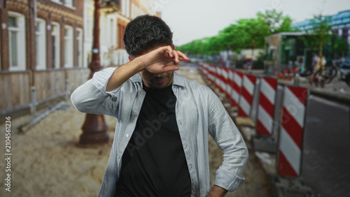 Принти на полотні Man smiling with hands on hips and eyes closed then rubbing his eye with forearm by construction barriers on a street; calm relief