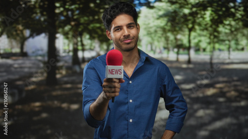 Obraz na płótnie Man holds red microphone out to camera with arm extended in a forest setting, smiling and engaging interviewer gesture; confidence reporting