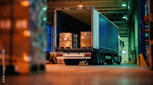 Loaded cargo truck parked at a warehouse loading dock with packaged goods stacked on pallets. Freight transportation and logistic delivery service for supply chain distribution, import export trade