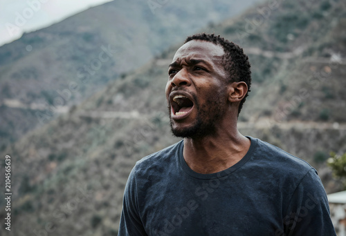 Anguished young black man shouting outdoors in mountains