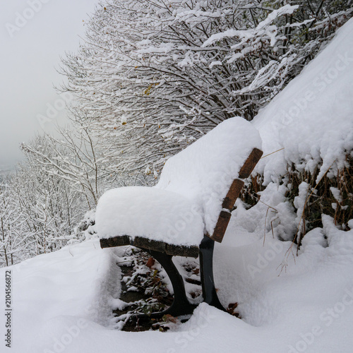 Empty park bench completely blanketed by soft winter snow.
