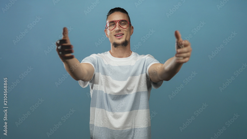 Naklejka premium Man points both index fingers to camera wearing red glasses and striped t shirt in studio; confidence invitation outreach.