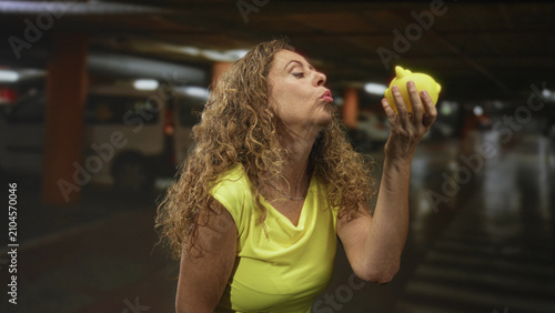 Fotografi Woman holding yellow piggy bank, finger to lips for silence and hand cupping coin slot in building; secrecy thrift contemplative