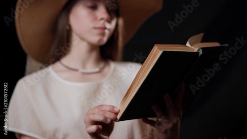 Konstfotografi Young woman reading hardcover book under wide-brim hat, hands and pages in foreg