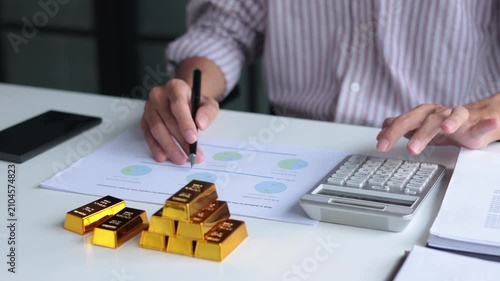 Close-up hands using calculator for gold bar trading analysis. Concept for wealth management, asset protection, and financial planning.