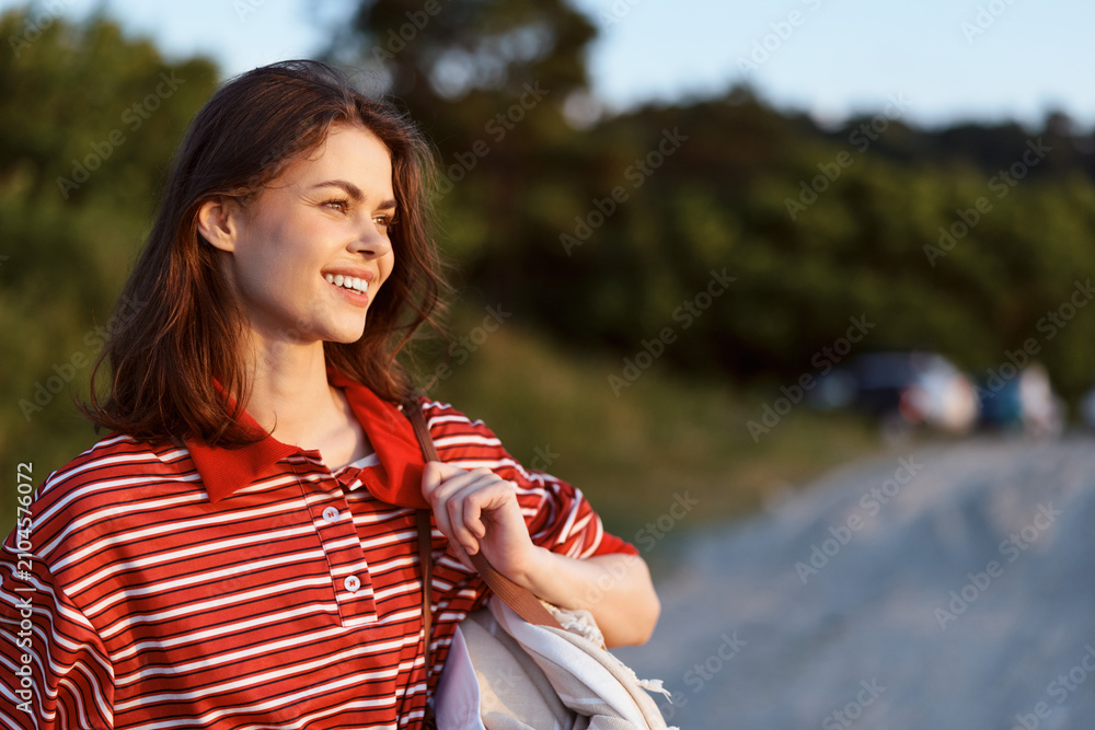 Obraz premium Smiling woman walking outdoors in casual clothes during sunny day. Lifestyle concept with happy person enjoying leisure time in nature. Soft golden hour light creates a natural warm mood.