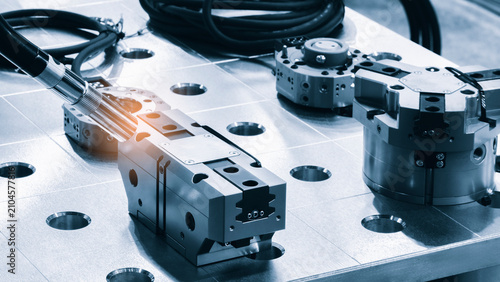 Industrial clamps and fixtures lie on a metal workbench. Black cables are coiled next to the workbench surface. tech industrial technology background