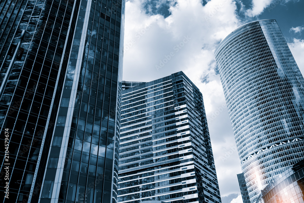 Obraz premium Tall glass skyscrapers of business offices in city reflect blue sky, clouds, and other skyscrapers. Sunlight glistens on glass surface. modern cityscape of city's business district.