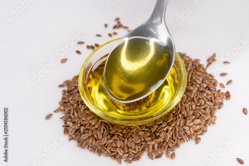 Fotografie Flax seeds oil dripping from a stainless steel spoon against a glass bowl and heap flax seeds
