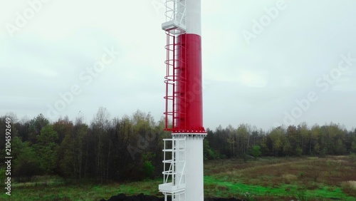 Foto Tall industrial tower with enclosed ladder beside forest edge