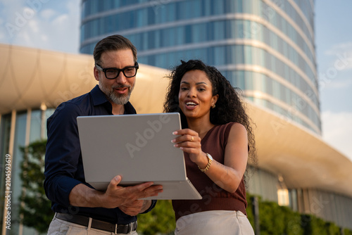 Successful business man and woman analyzing AI project performance outside corporate building in urban city district, reviewing digital results, strategy, innovation and teamwork
