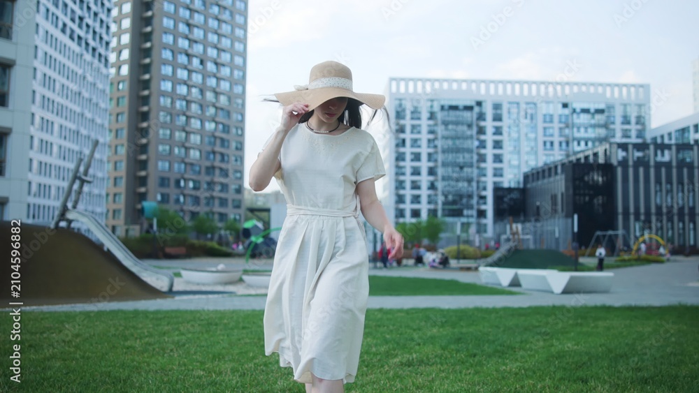 Fototapeta premium Woman walking across a city park in a light summer dress