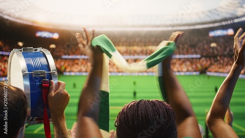 Photography Football supporters clap and beat a drum across packed stadium seats, applauding together during a loud match-day chant and creating coordinated crowd rhythm