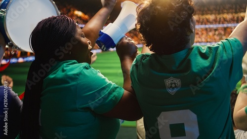 Canvas Print Woman uses a megaphone beside singing soccer fans in crowded stadium seats, leading football chants and shouting support for the team across the live sports arena during the match