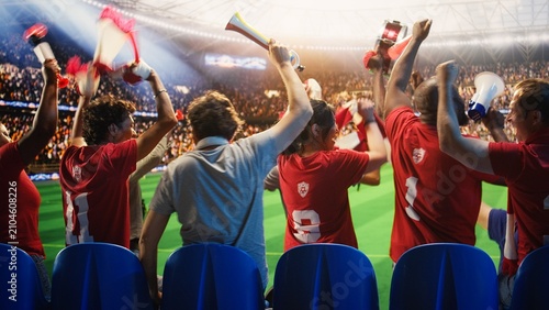 Fotografie Excited football supporter beats a drum while walking among fans in a packed stadium, leading loud crowd chants with vuvuzelas and a megaphone on match day