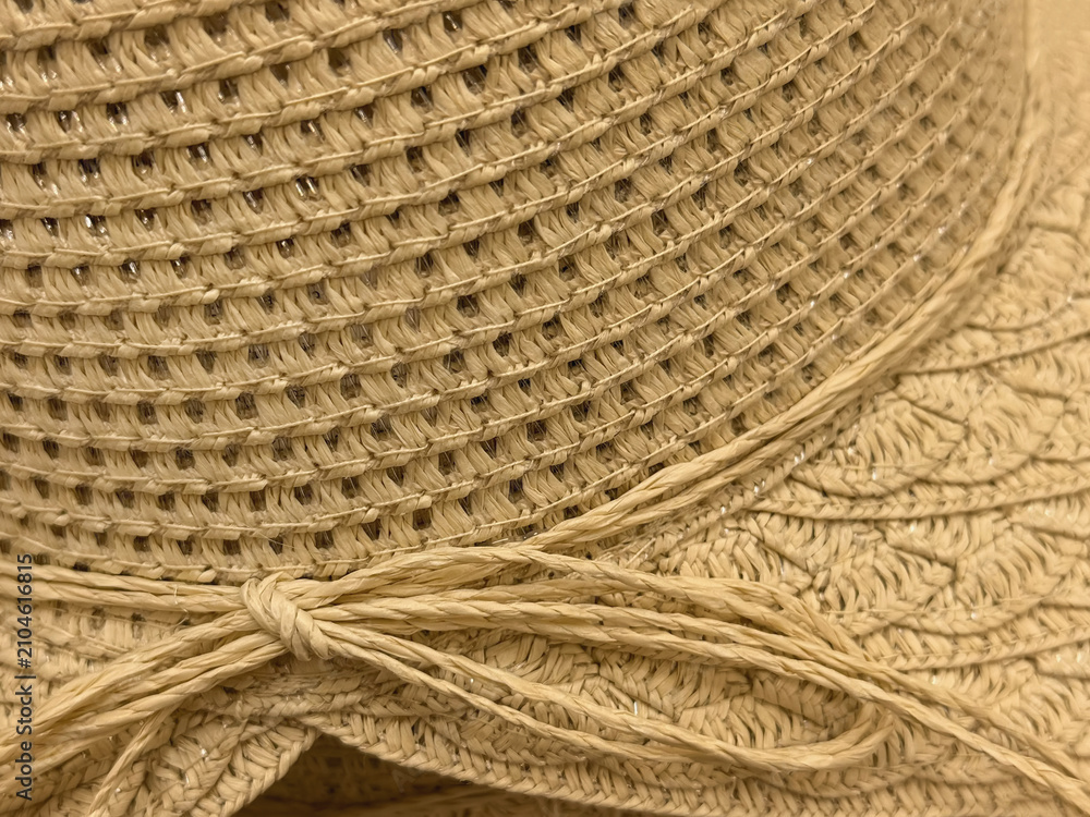 Obraz premium Close-up detail of beige woven sun hat with wide brim, decorative cord tied in bow. Natural summer fashion texture for vacation, beach accessories, handmade craft themes, copy space
