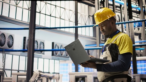 Εκτύπωση καμβά A smart solar panel factory technician uses a laptop to oversee conveyor belts; an African American man monitors machinery to maintain optimal efficiency during solar panel production